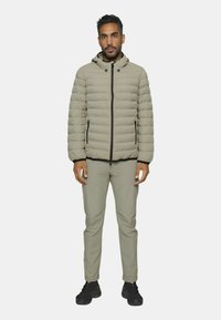 Gepolsterte Jacke in hellbeige mit Kapuze, durchgehendem Reißverschluss und schwarzen Akzenten. Kombiniert mit passenden hellbeigen Hosen und schwarzen Schuhen.
