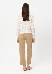 Cream floral-patterned knit sweater, tan straight-leg pants, beige woven slip-on shoes. Smooth texture, relaxed fit, and subtle color contrast.