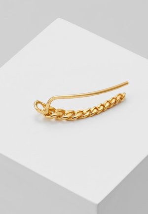 Bague d’oreille en chaîne dorée avec une fermeture à crochet courbé, présentée sur une surface blanche inclinée.