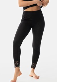Leggings noirs au design ajusté, fabriquées à partir d'un matériau lisse. Présentent une bordure en dentelle noire transparente à la cheville, ajoutant du détail et de la texture.