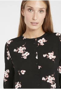 Zwarte button-up shirt met een bloemmotief in roze en wit. Heeft een ronde halslijn en lange mouwen, gemaakt van zachte stof.
