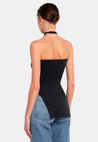 Top nero a fascia con corpetto aderente e orlo curvo. Realizzato in un tessuto morbido. Abbinato a jeans in denim azzurri a vita alta.