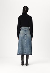 Denim midi suknja s blagim širenjem, svijetloplavog pranja i sirovim rubom, uparena s crnim kožnim čizmama do koljena.