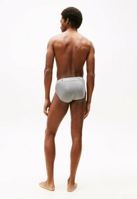 Un boxer gris avec une texture lisse, doté d'une ceinture contrastante. Le modèle est vu de dos, mettant en avant une silhouette athlétique.