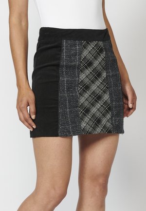 Jupe noire avec un panneau à carreaux texturé à l'avant, alliant des tissus unis et à motifs dans des tons sombres. Longueur mi-cuisse.