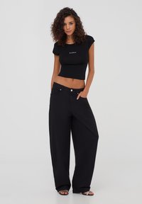 Una maglietta nera crop con un design aderente e un collo rotondo. Abbinata a jeans neri a gamba larga e sandali con punta aperta.