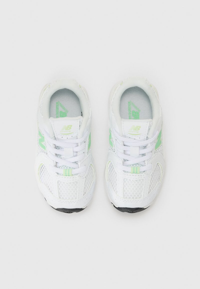 Baskets de sport blanches en tissu en maille avec des accents verts, présentant un design à lacets et une semelle en caoutchouc, vues de dessus.