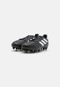 Botas de fútbol negras con material de cuero, que presentan una superficie texturizada y la marca de tres franjas en blanco. Equipadas con taquitos moldeados para tracción.