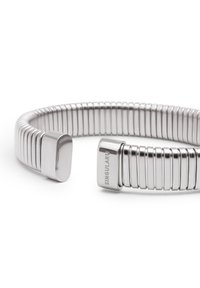 Bracciale in metallo argento con un design testurizzato a righe e estremità rettangolari lisce. Inciso con "SINGULAR" su un lato.