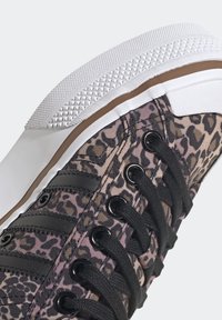 Baskets en toile à imprimé léopard avec œillets et lacets noirs, semelle en caoutchouc blanche et embout texturé. Présente des rayures noires sur le côté.