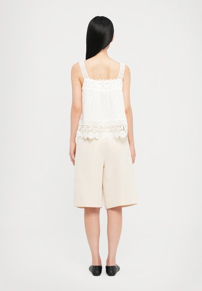 White lace tank top with floral accents and a textured back, paired with beige loose shorts and black slip-on shoes.