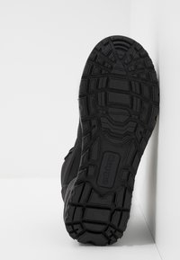 Svart atletisk sko sula med texturerat gummi för grepp, med ett geometriskt mönster och en logodetalj. Sidan visar en slank design.