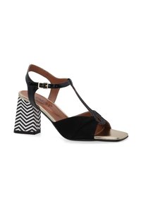 Schwarze hochhackige Sandalen mit einem T-Riemen-Design, ausgestattet mit einer goldenen metallischen Zehenpartie und einem gemusterten blockartigen Absatz in Schwarz und Weiß. Glattes Leder und Wildlederstruktur.