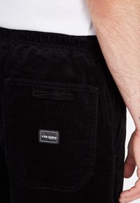 Jogging in corduroy neri con elastico in vita, dotati di una tasca posteriore con patch logo Volcom bianco e strisce verticali testurizzate.