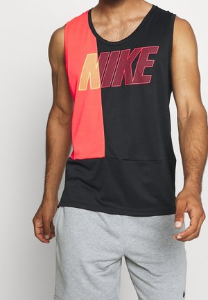 Mann trägt ärmelloses schwarzes und rotes Nike Tanktop mit großem Logo, kombiniert mit hellgrauen Shorts.