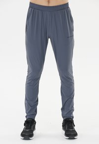 Graue Sporthosen mit elastischem Bund, schmalem Schnitt und seitlichen Taschen. Hergestellt aus leichtem, glattem Stoff. Schwarze Sneakers getragen.
