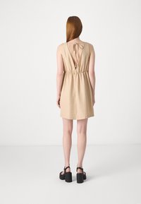 Beige linneklänning med en insydd midja, V-ryg och knytinformation. Matchad med svarta klacksandaler med tjock klack. Slät textur och enkel design.