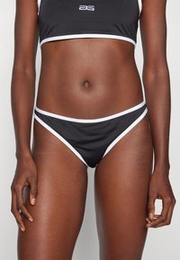 Bas de bikini noir avec des bordures blanches contrastées, présentant une coupe taille basse et un tissu lisse, conçu pour le confort et le maintien.