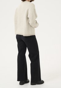 Woman wearing a cream and beige striped knit sweater, black wide-leg jeans, and black chunky boots, standing against a light background.