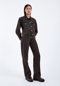 Braune Jeansjacke mit Brusttaschen und silbernen Knöpfen; kombiniert mit passenden braunen Schlagjeans und schwarzen Plateaustiefeln.