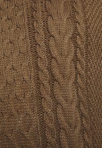 Hnědá pletená tkanina se vzorem copánku, střídající se zkroucené a křížové motivy, které zdůrazňují texturu a hloubku.