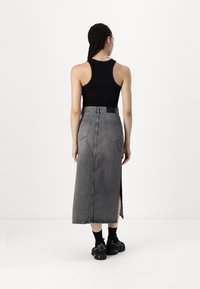 Schwarzes Tanktop kombiniert mit einem langen, grauen Denimrock, der einen seitlichen Schlitz und Taschen hat, getragen mit schwarzen Sneakers.