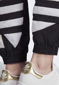 Vita sneakers med guld accenter, parat med svart och vit randig byxor med en krinklad textur och elastiska manschetter.