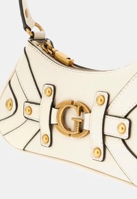 Biała skórzana torebka wyposażona w złote okucia, zapięcie na zamek oraz kontrastujące czarne przeszycia. Projekt zawiera ozdobne paski i ćwieki.