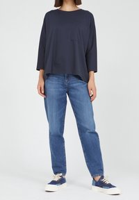 Tummansininen, löysä pitkähihaiset paita, jossa on rintatasku, yhdistettynä vaaleansinisiin suoriin farkkuihin ja sinivalkoisiin lenkkareihin.