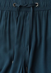 Pantalon bleu foncé avec une taille élastique et de longs cordons attachés par des œillets métalliques.
