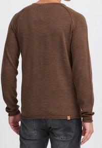 Brun långärmad tröja med en texturerad stickad mönster, rund halsringning och ribbade ärmslut. Har en liten läderlogotyp vid fållen.