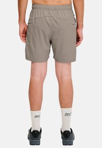 Beiga shorts med elastisk midja, med sidofickor och ett lätt, vattenavvisande material. Bärs med grå sneakers och vita strumpor.