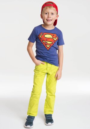Blue T-shirt with a large red and yellow Superman logo, paired with bright yellow pants and navy sneakers. Child wearing a red cap.