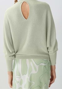 Helle grüne Strickpullover mit einem Schlüsselaugen-Detail auf dem Rücken, überschnittenen Schultern und gerippten Bündchen, kombiniert mit einem gemusterten mintgrünen Rock.