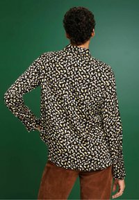 Zwarte blouse met een kleurrijk, abstract luipaardpatroon in crème en geel. Lange mouwen met knoopmanchetten, relaxed fit en zachte textuur.
