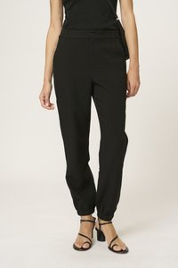 Black trousers with a tailored design, featuring a button closure, elastic cuffs, and smooth texture. Paired with strappy black heels.