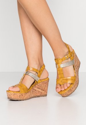 Sandales compensées jaunes avec une finition texturée, des accents argentés et une plateforme en liège. Bride de cheville réglable avec détail boucle.