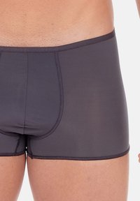 Boxer in colore nero realizzati in un tessuto liscio e elastico. Presentano una forma aderente con una tasca definita e un elastico in vita a contrasto.