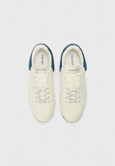 Baskets blanches avec des accents bleus, design à lacets, matériau lisse et détails de logo sur le côté et les lacets. Bout arrondi et semelle plate.