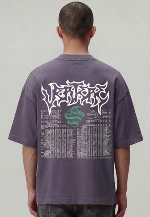 Paars T-shirt met korte mouwen, witte gestileerde tekst en een groene slangengrafiek op de achterkant, gedragen door een persoon die van zich af kijkt.