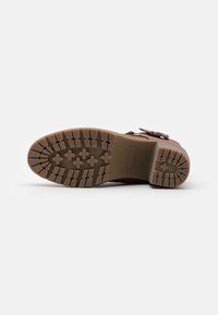 Semelle de chaussure brune avec un motif en caoutchouc texturé, présentant des formes croisées et des rainures pour la traction. Comprend des marquages de marque et de taille.