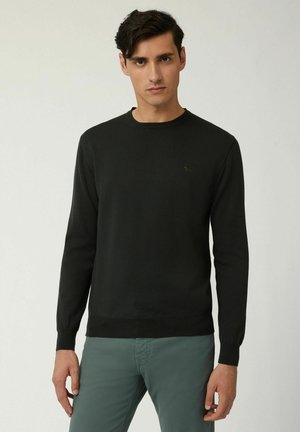 Maglione nero a maglia con colletto rotondo, maniche lunghe e polsini a costine; presenta un piccolo logo verde sul petto; trama liscia.