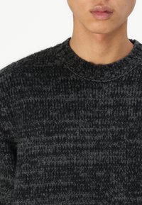 Pull en maille épaisse de couleur gris foncé, avec un col rond et un motif texturé, offrant une finition douce et chaude.