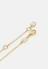 Gouden ketting met een dunne ketting, voorzien van een cirkelvormig schakeldesign en een centrale facetrijpe heldere steen. Inclusief een carabijnsluiting.