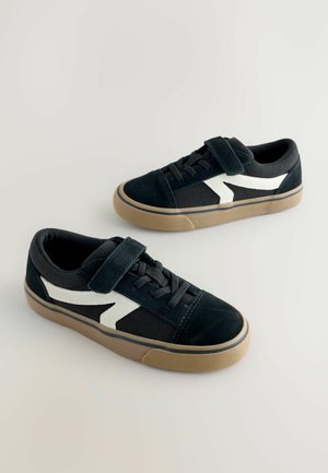 Baskets en daim noir avec un motif en zigzag blanc, dotées d'une bride Velcro et de lacets, ainsi que d'une semelle en caoutchouc colorée pour une bonne adhérence.