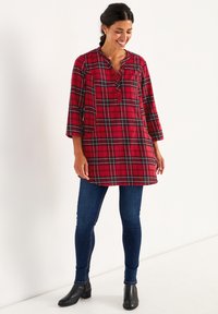 Rødternet tunika med trekvartærmer, knaplukning, to forlommer, parret med mørke skinny jeans og sorte ankelstøvler.