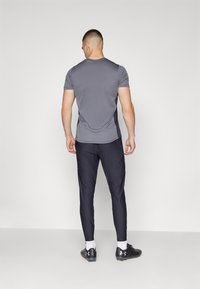 Grå atletisk T-shirt med korte ærmer, parret med mørke tætsiddende bukser og sorte sportssko. Glat tekstur, minimalistisk design.