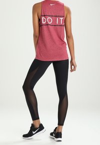 Punainen urheilullinen tank top, jossa on "TEHKÄÄ SE" teksti, yhdistetty mustiin leggingseihin, joissa on verkko paneelit, sekä mustiin lenkkareihin. Minimalistinen design.