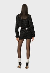 Zwarte tweed cropped jasje met rafelige randen, gecombineerd met een bijpassende minirok. Model draagt doorschijnende panty’s en zwart-witte hoge hakken.
