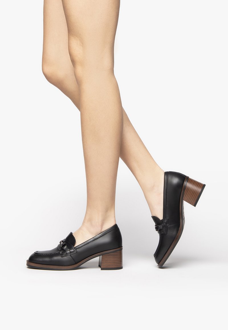 Scarpe in pelle nere con punta arrotondata, tacco basso, accenti decorativi a fibbia e dettagli in legno testurizzato sul tacco.